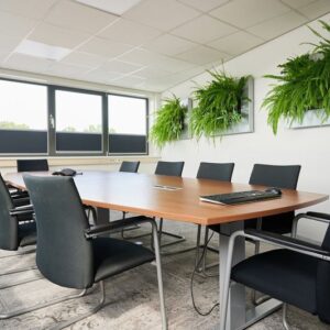 Vergaderruimte met ergonomische stoelen, houten tafel en groene wandplanten – een voorbeeld van duurzame en impactvolle projectinrichting.