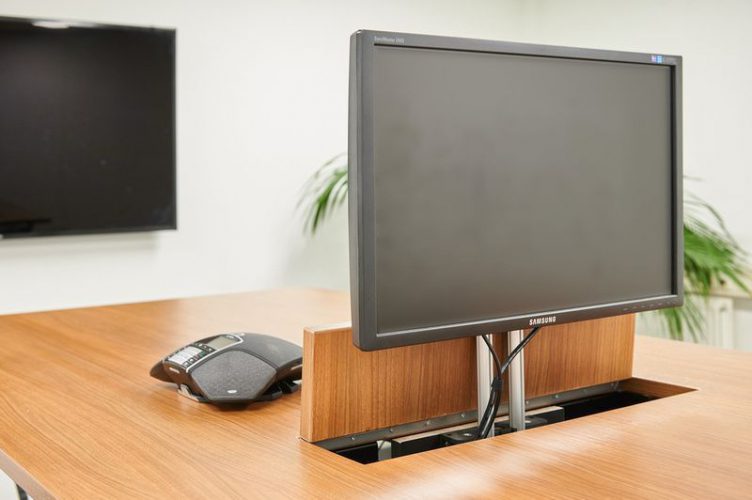 Detail van ingebouwde monitor en ergonomische muis op houten tafel – technologische integratie in moderne projectinrichting.