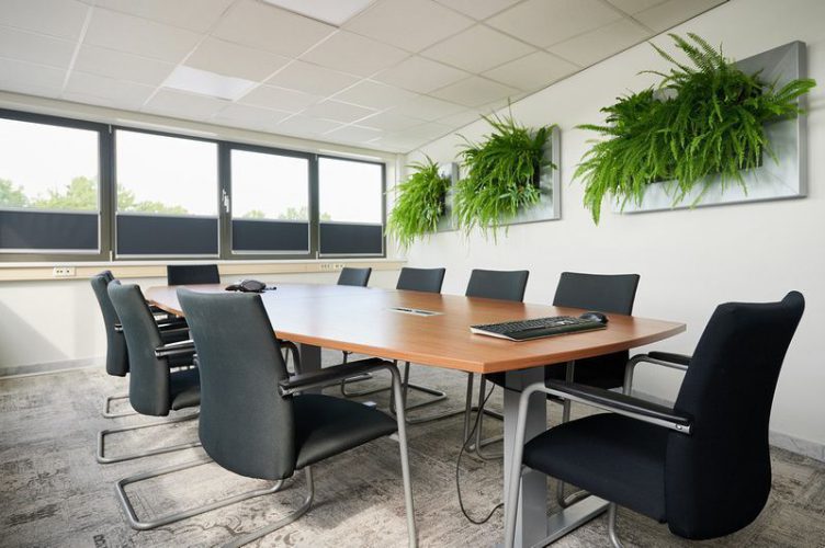 Vergaderruimte met ergonomische stoelen, houten tafel en groene wandplanten – een voorbeeld van duurzame en impactvolle projectinrichting.